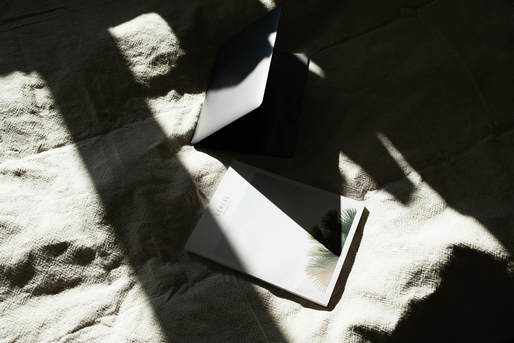 From above of opened laptop and book placed together on soft blanket on bed in light bedroom in daylight